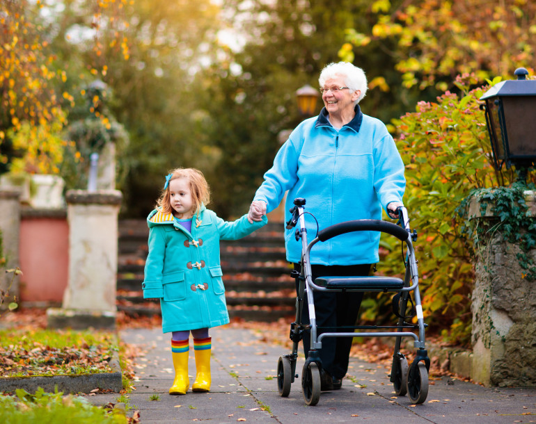 Grandmother holding hands with child while using a walking aid