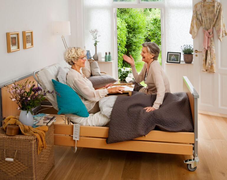 Two happy women having a conversation in a bedroom with a reclining bed.